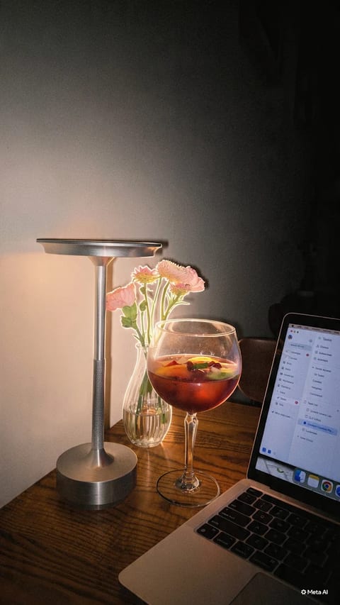 A glass of sangria beside flowers, a table lamp and a laptop at Luna